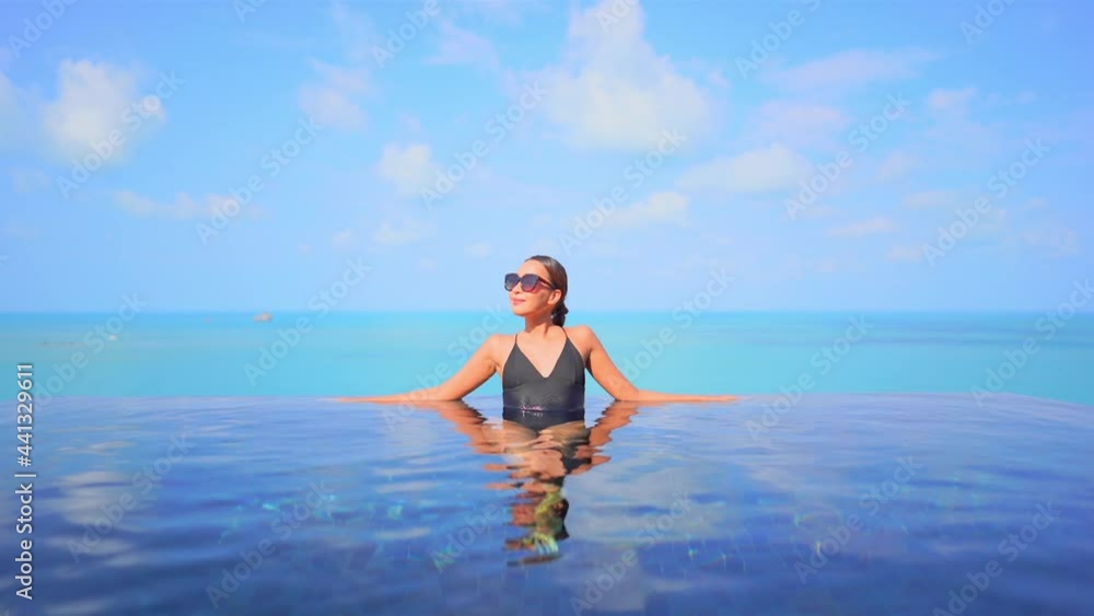 An attractive young woman leans along the edge of an infinity-edge pool with an ocean horizon in the background. Title space An attractive young woman leans along the edge of an infinity-edge pool with an ocean horizon in the background. Title space