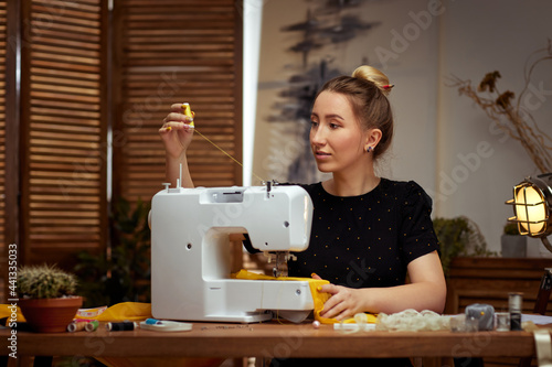 Beautiful young seamstress working on sewing machine photo