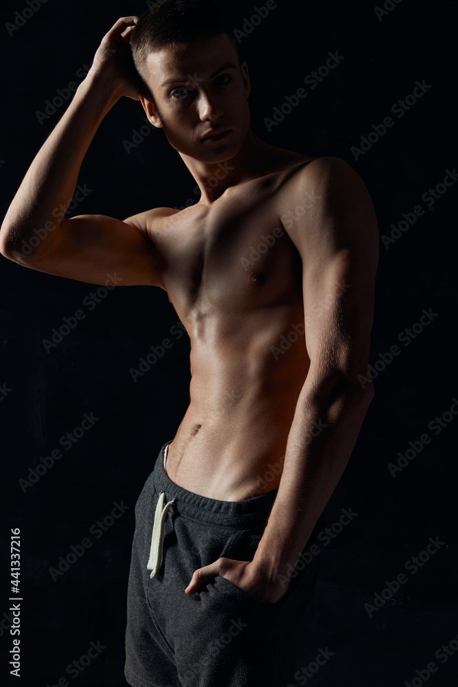 Fototapeta premium athlete with an inflated torso in gray pants holds his hand near his face on a black background