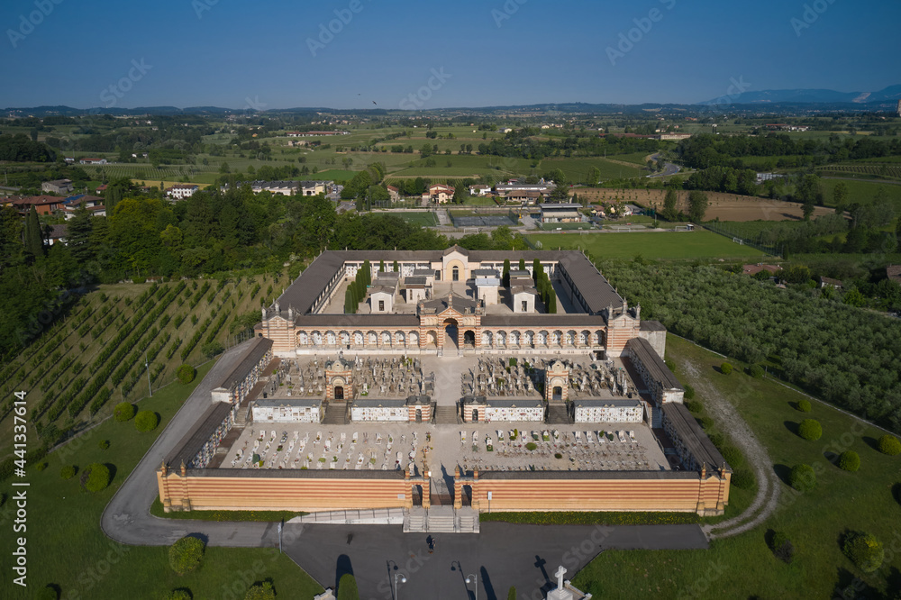 Obraz premium Top view of a cemetery located near olive trees and vineyards in Italy. Traditional Italian cemetery, Cimitero di Pozzolengo, aerial view. Burial place in Italy top view.