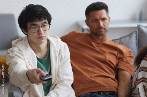 Portrait of young Asian man holding TV remote while watching movies with friends and family at home