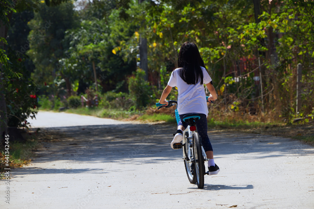 Child bike on local road outdoor activity. Back view of Asian child biking along country road in summer time.