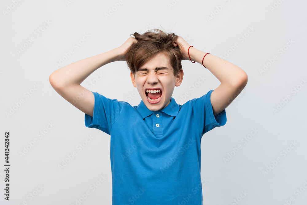 Frustrated boy with eyes closed, messing up and pulling his hair, hands to head shouting and screaming Frustrated boy with eyes closed, messing up and pulling his hair, hands to head shouting and screaming