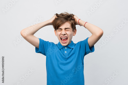 Frustrated boy with eyes closed, messing up and pulling his hair, hands to head shouting and screaming