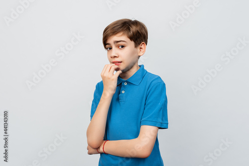 Frightened teen boy biting fingernails and looking at camera with anxious face