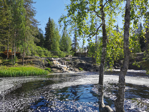 The picturesque waterfalls on the Tokhmayoki River  on the bank of which there is a wooden house  are all surrounded by Karelian nature. 