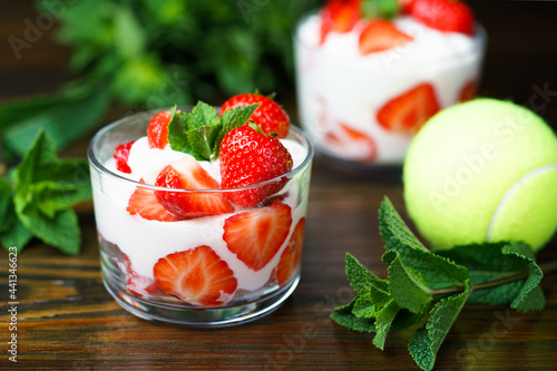 Whipped cream and strawberries served in a glass. Dark wooden table, tennis ball in bokeh, high resolution