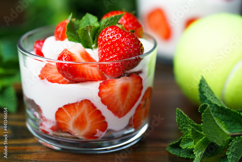 Whipped cream and strawberries served in a glass. Dark wooden table, tennis ball in bokeh, high resolution