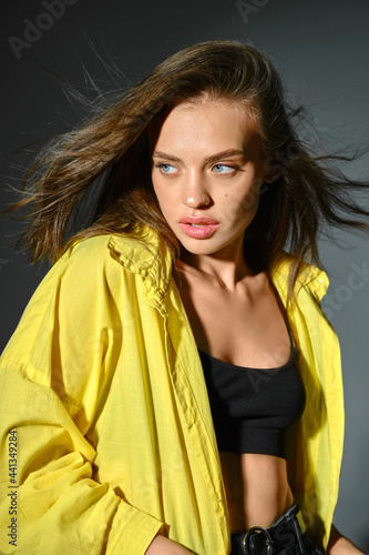 Young woman in yellow shirt with flying brown hair on grey background