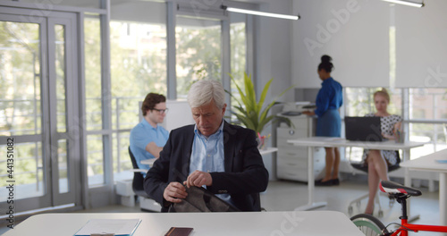 Mature executive sitting at desk and opening bag in coworking office 