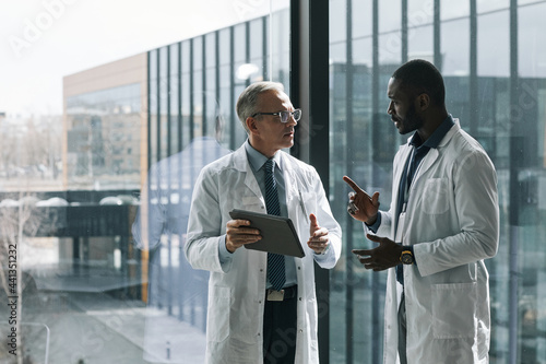 Konstfotografi Waist up portrait of two doctors talking while standing by window in conference