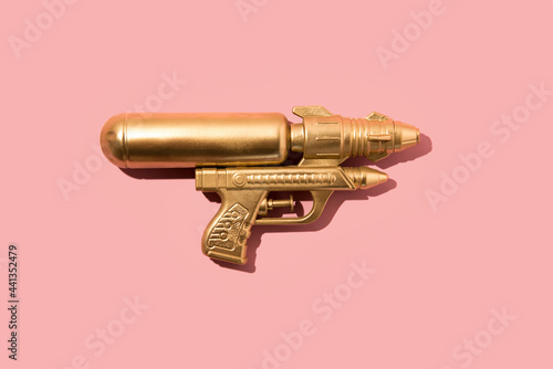 Gold hipster watergun or handgun on pink pastel background. Minimal flat lay concept.