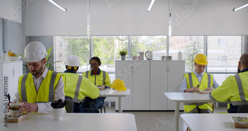 Group of young industrial workers eating takeaway lunch at modern office canteen