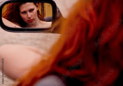 Reflection of a young redhead woman with wild red hair in the car mirror