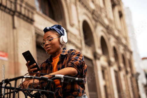 Happy young woman riding bicycle in the city. Beautiful african woman using the phone outdoors..
