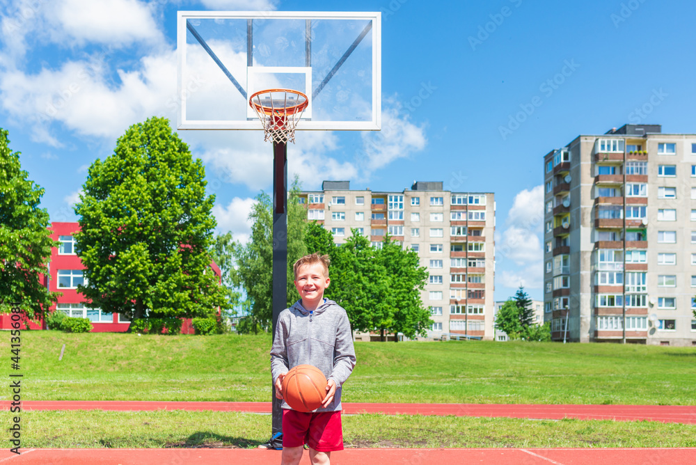 Young kid playing basketball on playground.Boy performs shot at basketball game on the playground during summer day.