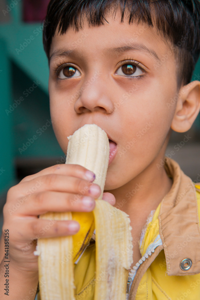 Indoor image of an Asian, Indian cute little boy in yellow clothes eating a fresh banana at home. Indoor image of an Asian, Indian cute little boy in yellow clothes eating a fresh banana at home.