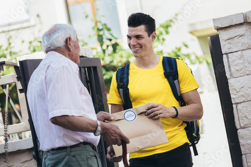 Young male volunteer delivering shopping to senior man. Donation