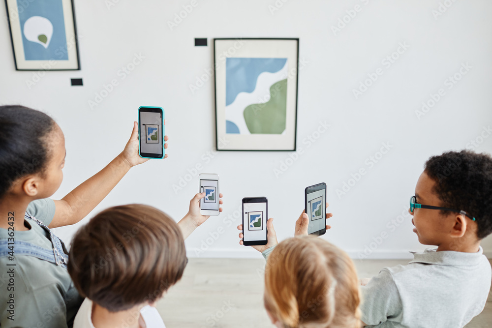 Obraz premium High angle view at diverse group of children holding smartphones in art gallery and taking photos of paintings, digital world, copy space