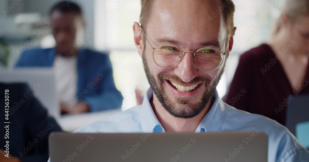 Portrait of smiling businessman sitting at desk with laptop in modern open plan office Portrait of smiling businessman sitting at desk with laptop in modern open plan office