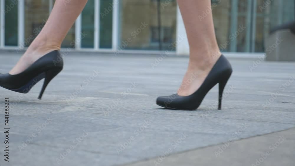 Feet of young businesswoman in footwear on high-heeled going in urban street. Slim female legs in black shoes on high heels walking on city. Girl stepping to work. Low angle view Slow motion Close up Feet of young businesswoman in footwear on high-heeled going in urban street. Slim female legs in black shoes on high heels walking on city. Girl stepping to work. Low angle view Slow motion Close up