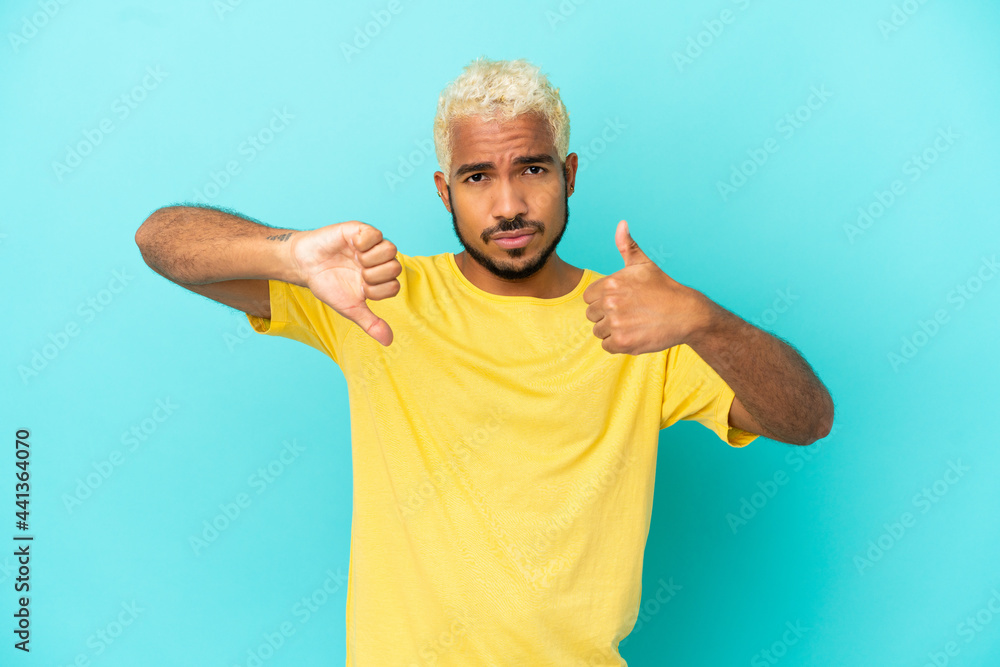 Young Colombian handsome man isolated on blue background making good-bad sign. Undecided between yes or not Young Colombian handsome man isolated on blue background making good-bad sign. Undecided between yes or not