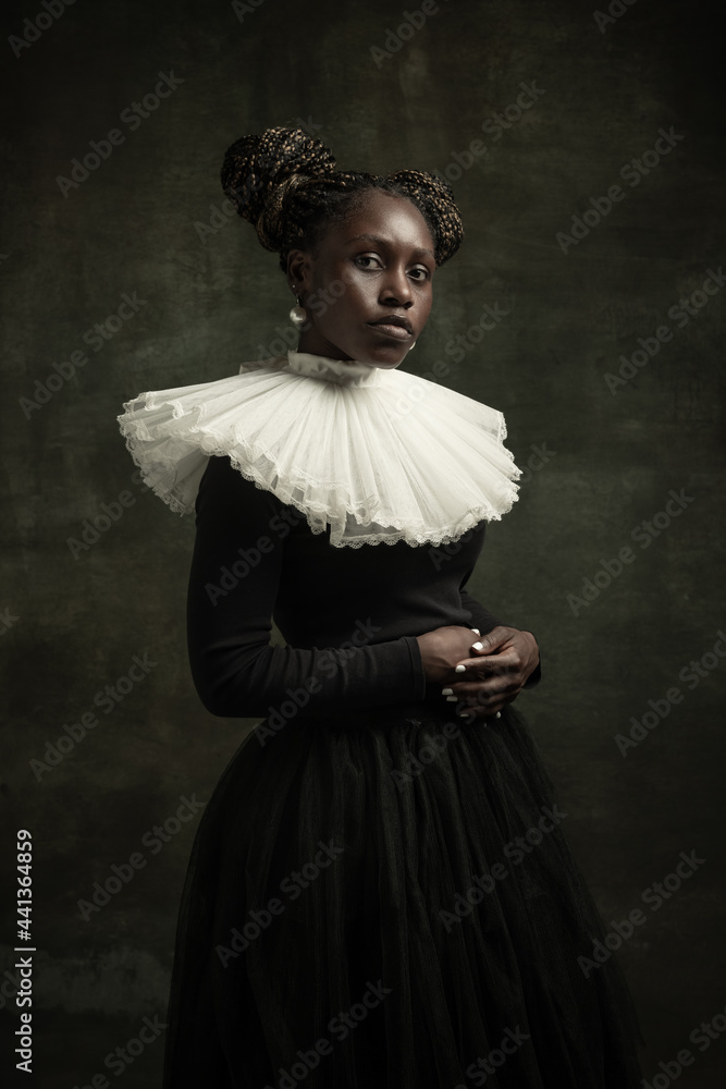 Portrait of medieval African young woman in black vintage dress with big white collar posing isolated on dark green background.