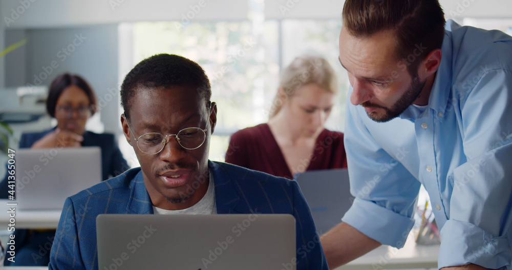 Young African businessman showing information on laptop to colleague Young African businessman showing information on laptop to colleague