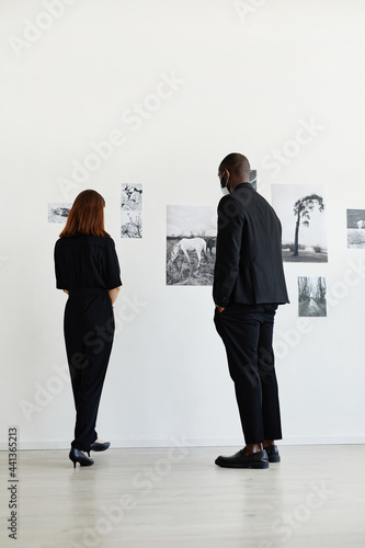Minimal back view at two people wearing black while looking at photographs in modern art gallery © Seventyfour