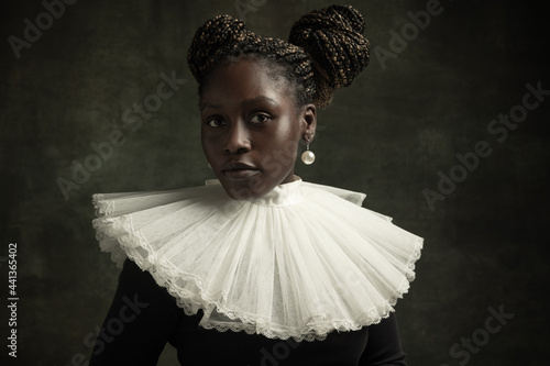 Close-up portrait of medieval African young woman in black vintage dress with big white collar posing isolated on dark green background.