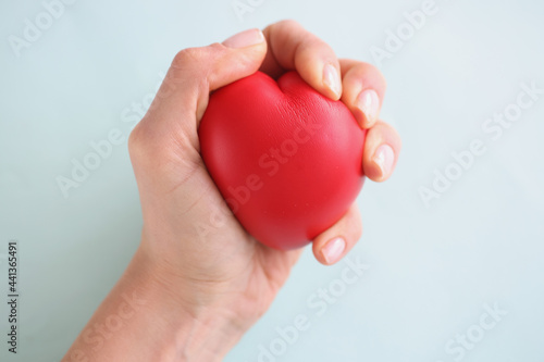 Fototapeta Naklejka Na Ścianę i Meble -  Female hand holding red toy heart on blue background closeup