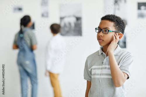 Waist up portrait of young African-American boy looking at paintings in modern art gallery, copy space