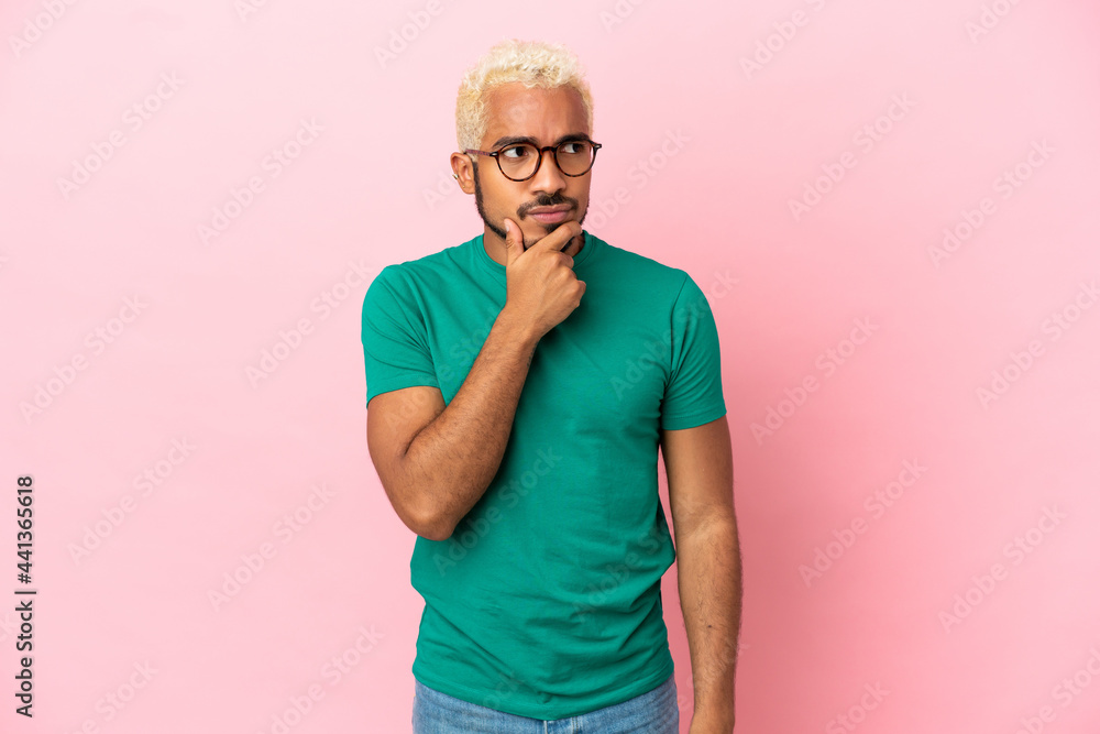 Young Colombian handsome man isolated on pink background having doubts and with confuse face expression Young Colombian handsome man isolated on pink background having doubts and with confuse face expression