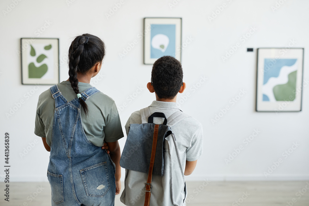 Fototapeta premium Back view at two schoolchildren visiting art gallery and looking at modern abstract paintings, copy space