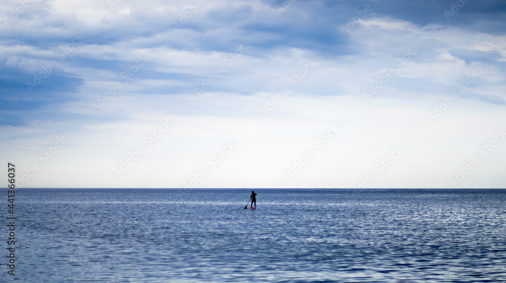 One man achieving balance while paddle surfing in calm waters of de mediterranean sea before it start to rain