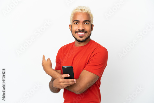 Young Colombian handsome man isolated on white background using mobile phone and pointing back © luismolinero