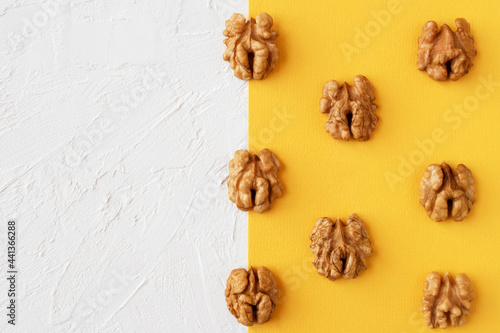 Halves of walnuts on yellow and white background, flat lay.