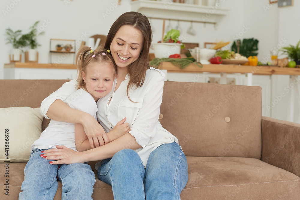 The little girl complains to her mother and cries. A young woman calms her daughter on the couch at home The little girl complains to her mother and cries. A young woman calms her daughter on the couch at home