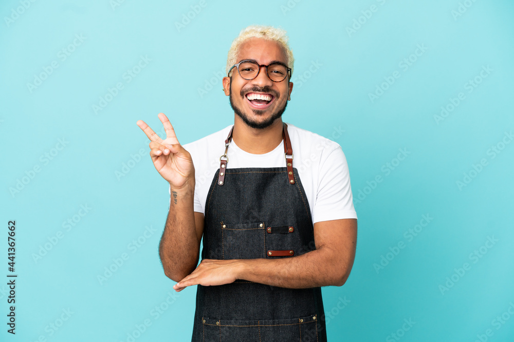 Restaurant Colombian waiter man isolated on blue background smiling and showing victory sign Restaurant Colombian waiter man isolated on blue background smiling and showing victory sign