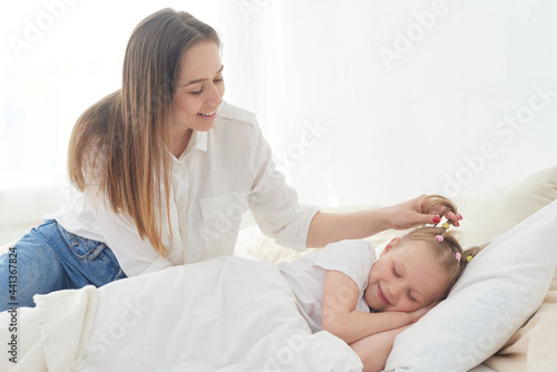 Beautiful young mom wakes up her preteen little daughter in the morning. Tenderness and care. Mother's love