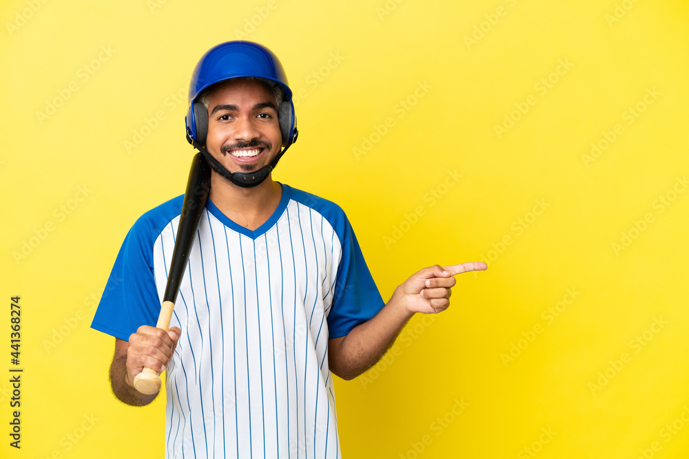 Young Colombian latin man playing baseball isolated on yellow background pointing finger to the side Young Colombian latin man playing baseball isolated on yellow background pointing finger to the side
