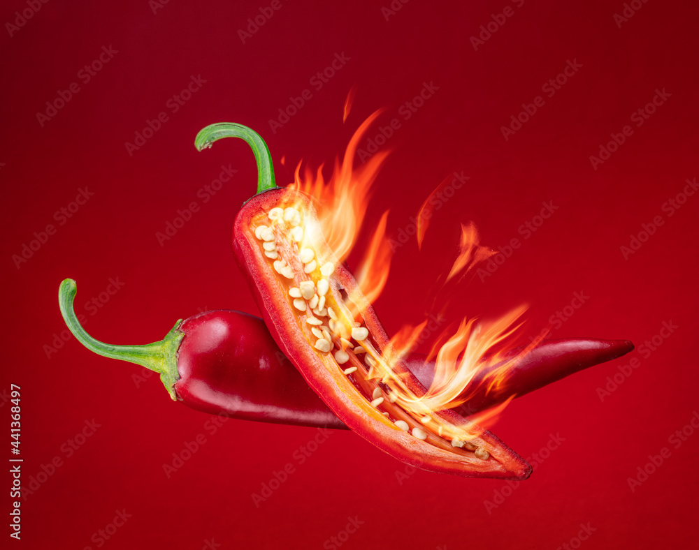 Fresh red chilli pepper in fire as a symbol of burning feeling of spicy food and spices. Red background. - obrazy, fototapety, plakaty 