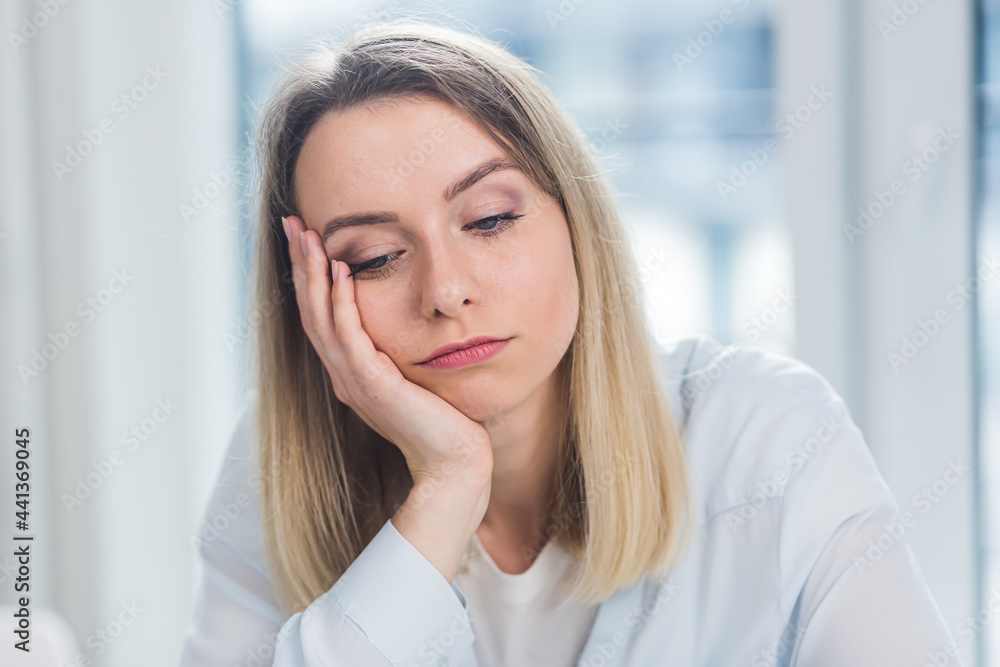 Close-up portrait of a young adult blonde business woman looking at the camera indoors at office or home on a blue window background. Face Confident female Manager in Formal Wear indoors Close-up portrait of a young adult blonde business woman looking at the camera indoors at office or home on a blue window background. Face Confident female Manager in Formal Wear indoors