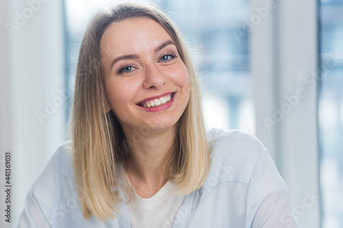 Close-up portrait a caucasian young blonde woman indoors looking at camera and smiling. Cute Happy Female in the office or at home with makeup and a beautiful smile and blue eyes. Closeup