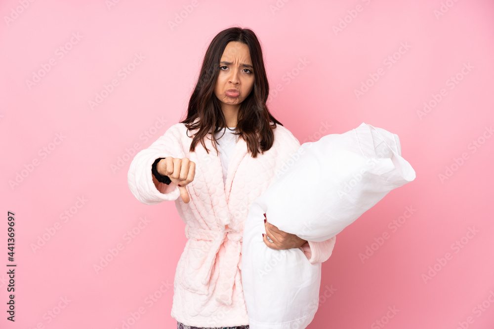 Young woman in pajamas isolated on pink background showing thumb down with negative expression Young woman in pajamas isolated on pink background showing thumb down with negative expression