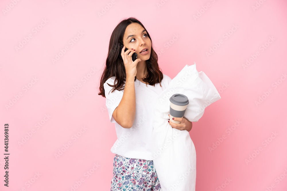 Young woman in pajamas isolated on pink background holding coffee to take away and a mobile Young woman in pajamas isolated on pink background holding coffee to take away and a mobile