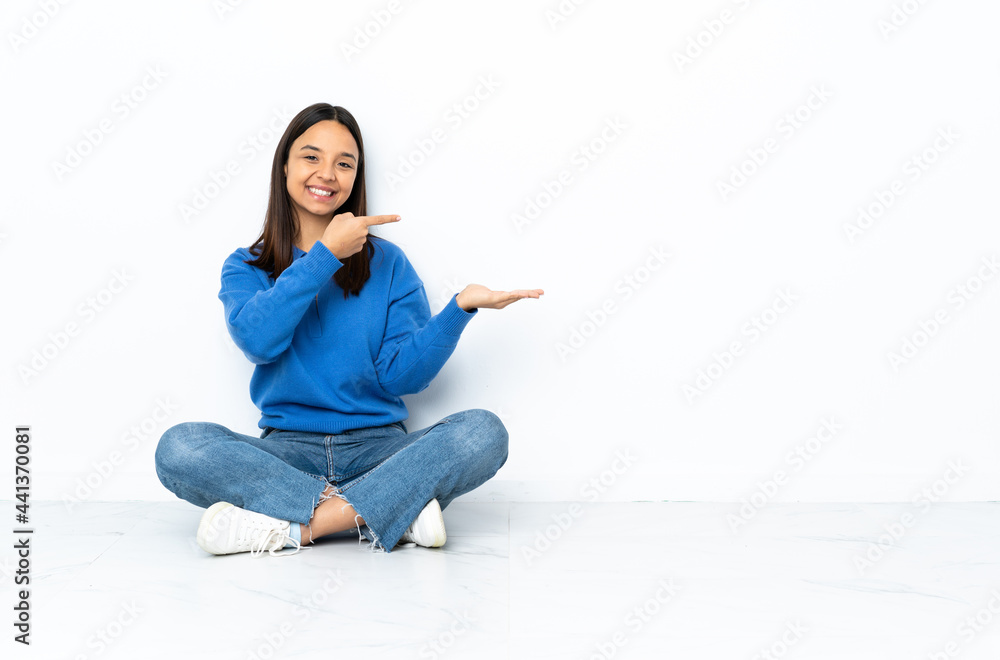 Young mixed race woman sitting on the floor isolated on white background holding copyspace imaginary on the palm to insert an ad Young mixed race woman sitting on the floor isolated on white background holding copyspace imaginary on the palm to insert an ad