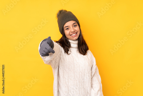 Young woman with winter hat over isolated yellow background with thumbs up because something good has happened © luismolinero