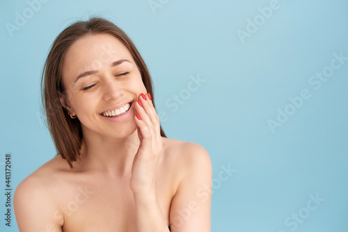Smiling woman touching her face against a blue background. Natural beauty concept, happy woman