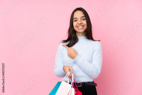 Young woman with shopping bag over isolated pink background pointing to the side to present a product
